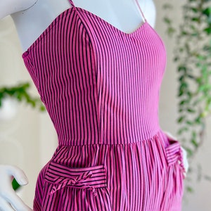 May include: Pink and black striped jumpsuit with a sweetheart neckline and two pockets. The pockets have a decorative bow detail.