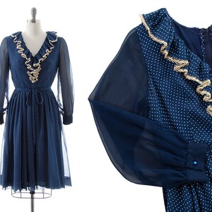 May include: A blue and white polka dot dress with a ruffled collar and long sleeves. The dress has a fitted bodice and a flowing skirt.