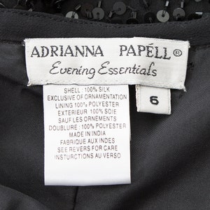 Puede incluir: Una etiqueta blanca con texto negro que dice "ADRIANNA PAPELL Evening Essentials" y enumera el contenido de la tela y las instrucciones de cuidado. La etiqueta est&aacute; unida a una prenda negra con lentejuelas.