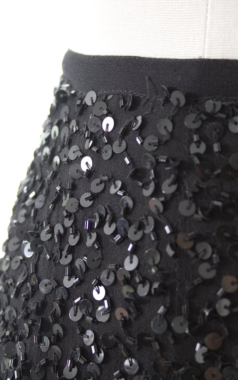 Puede incluir: Una falda negra con un dise&ntilde;o de lentejuelas. Las lentejuelas son peque&ntilde;as y redondas, y est&aacute;n dispuestas en un patr&oacute;n aleatorio. La falda est&aacute; hecha de una tela suave y fluida.