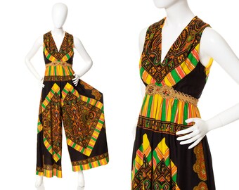 May include: A vintage jumpsuit with a V-neck and wide legs. The black fabric is accented with a colorful paisley and striped pattern in shades of orange, yellow, green, and gold. A gold-colored belt cinches the waist.