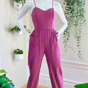 May include: A pink and black striped jumpsuit with a sweetheart neckline and cuffed legs. The jumpsuit has pockets on the front and is on a white mannequin.