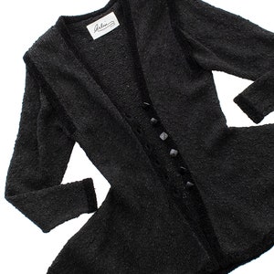 May include: A black fuzzy cardigan with a V-neck and a row of black buttons down the front. The cardigan has a flared hem and a label that reads "Arlin".