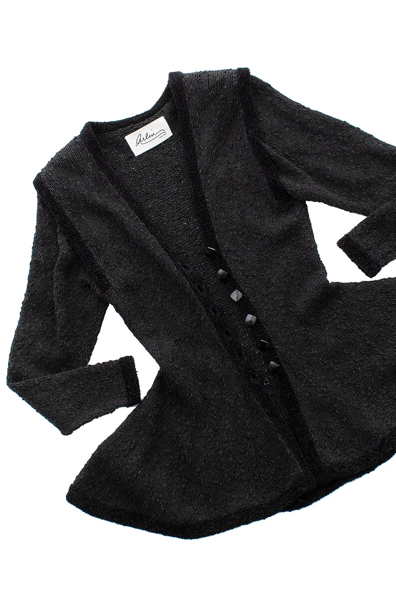 May include: A black fuzzy cardigan with a V-neck and a row of black buttons down the front. The cardigan has a flared hem and a label that reads "Arlin".