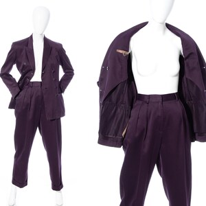 Pu&ograve; includere: Un completo viola con una giacca doppiopetto e pantaloni abbinati. La giacca ha una fodera marrone e i pantaloni hanno pieghe.