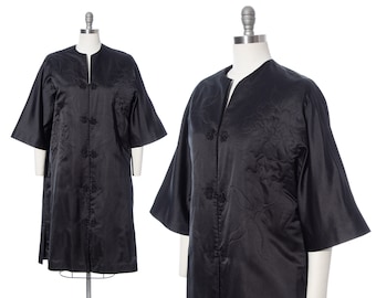 May include: A black satin robe with embroidered floral details and a mandarin collar. The robe has a long, flowing silhouette and is fastened with buttons down the front.