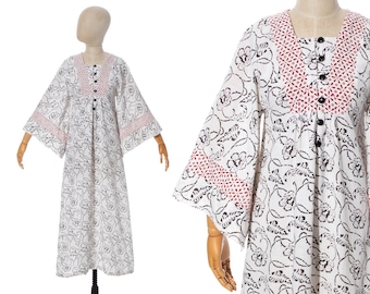 May include: A white cotton maxi dress with a black floral print and red geometric trim. The dress has a button-up front and bell sleeves.