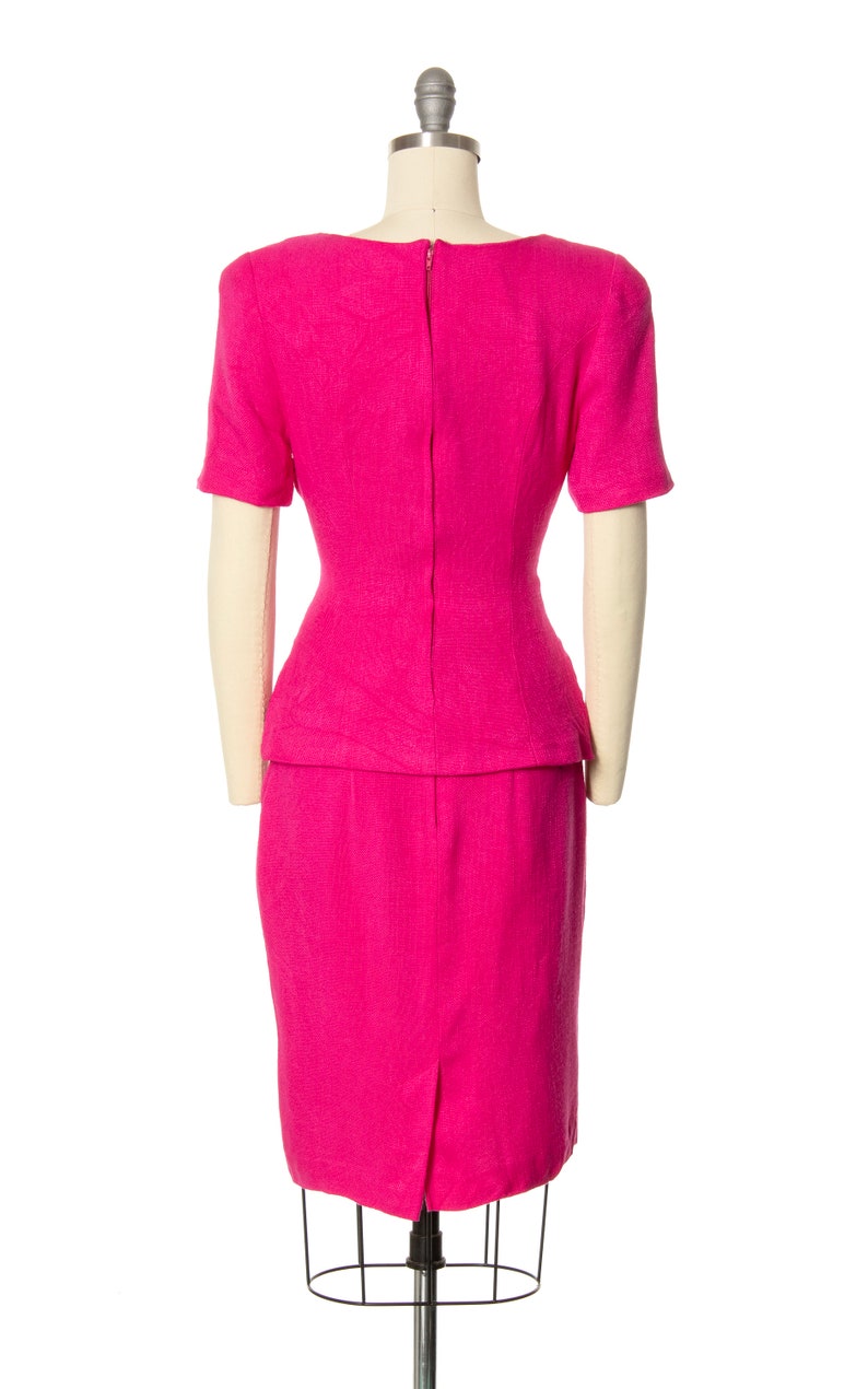 May include: A hot pink dress with a fitted bodice and a skirt that falls to the knee. The dress has a back zipper and short sleeves.