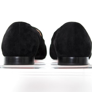 May include: A pair of black suede loafers with a pointed toe and a low heel. The loafers are sitting on a white surface.