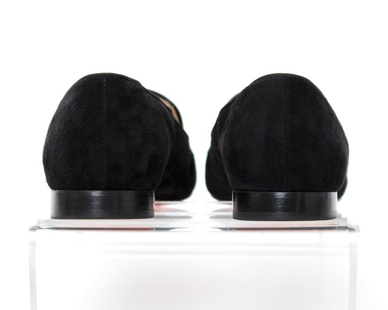 May include: A pair of black suede loafers with a pointed toe and a low heel. The loafers are sitting on a white surface.