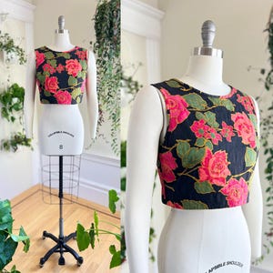 May include: A black sleeveless crop top with a floral print featuring pink roses and green leaves. The top is on a white mannequin.