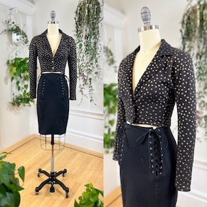 May include: A black cropped blazer with gold star print and a matching black skirt with lace-up detailing.