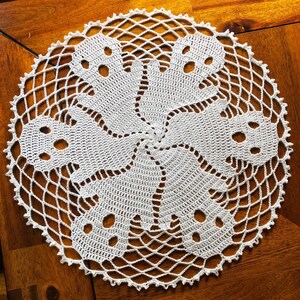 May include: A handmade, white crochet doily with a circular design. The doily features a central motif of six repeating floral-like shapes, each with three small holes. The outer edge has a delicate, openwork pattern.