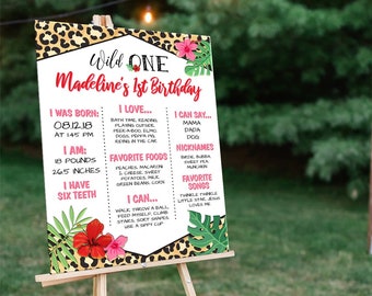 Może przedstawiać: Tablica z tropikalnym motywem w czarno-różowym wzorze lamparta. Na tablicy widnieje napis "Wild One Madeline's 1st Birthday" i zawiera informacje o dziewczynce obchodzącej urodziny, takie jak data urodzenia, waga, wzrost, ulubione jedzenie i piosenki. Tablica ma wymiary 45,7 cm na 61 cm.