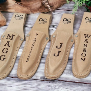 May include: Four brown leather knife sheaths with different names engraved on them: MAGG, DIAMONDZ RANCH, JJ, and WASSON. Each sheath has a brown leather strap with the text "CLC WORK GEAR NO. 767" printed on it.