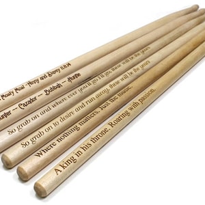 May include: Six wooden drumsticks with personalized messages engraved on them. The messages include names, dates, and inspirational quotes.