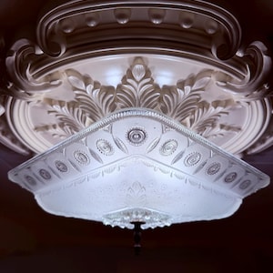 May include: A decorative ceiling light fixture with a frosted glass shade featuring floral and geometric patterns. The fixture is mounted on a detailed, ornate ceiling medallion with a white finish.