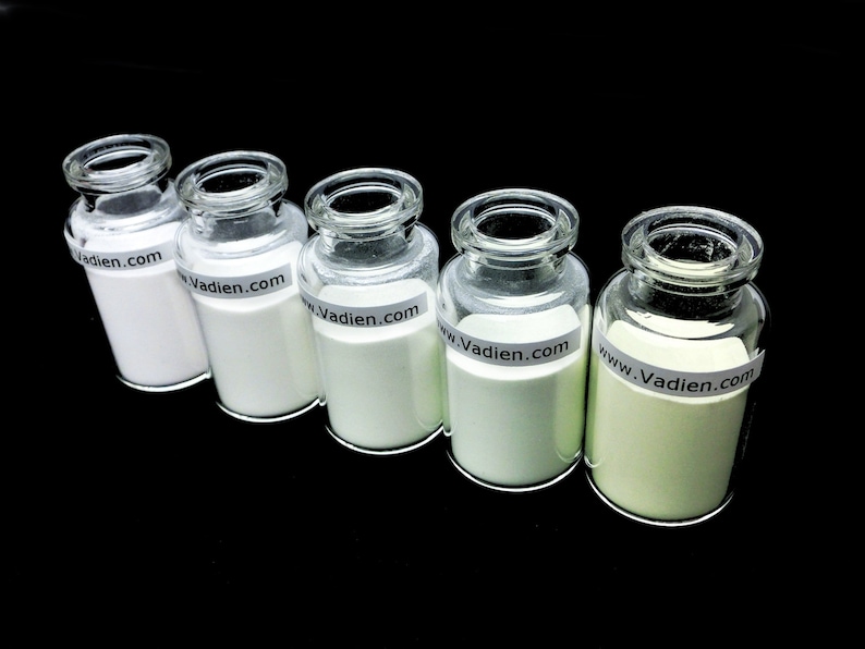 May include: Five glass jars with white powder inside. The jars have a white label with the text "www.Vadien.com" on them. The jars are arranged in a row from left to right, with the powder in each jar becoming progressively greener.