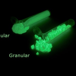 May include: Two test tubes filled with glowing green powder. The test tube on the left is labeled "Regular" and the test tube on the right is labeled "Granular".