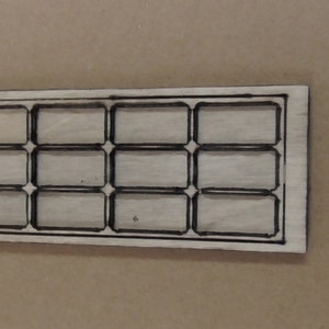 Peut inclure: Une découpe en bois d'une fenêtre avec un cadre rectangulaire et 12 petits carreaux rectangulaires. La découpe est de couleur brun clair avec des lignes noires délimitant le cadre et les carreaux.