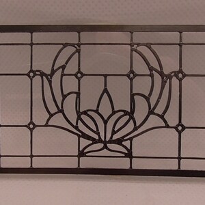 Op de afbeelding: Een zwart metalen glas-in-lood raam paneel met een geometrisch ontwerp met een gestileerde bloem in het midden.