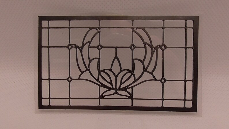 Op de afbeelding: Een zwart metalen glas-in-lood raam paneel met een geometrisch ontwerp met een gestileerde bloem in het midden.