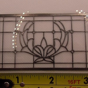 Puede incluir: Una plantilla de patrón de ventana de vitral de metal plateado que mide 7,6 cm de ancho. La plantilla presenta un diseño decorativo con un motivo floral.