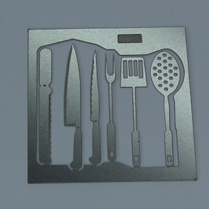 May include: A silver metal kitchen utensil holder with cutouts of a knife, a serrated knife, a fork, a spatula, and a slotted spoon.