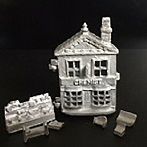 May include: A white miniature model of a building with a sign that reads "Chemist". The building has two windows and a door. The model is made of plaster and is about 4 inches tall.