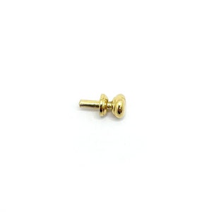 May include: A small, gold-coloured furniture knob. It features a cylindrical post and a rounded, oval-shaped head. The knob has a simple, classic design and is set against a plain white background.
