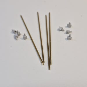 May include: Four gold-colored metal rods and several small, white, metal pieces on a white surface.