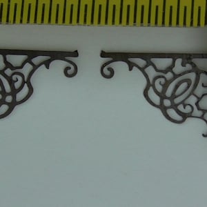 Puede incluir: Dos soportes de esquina de metal negro con un diseño floral decorativo. Los soportes miden aproximadamente 5 cm de largo.