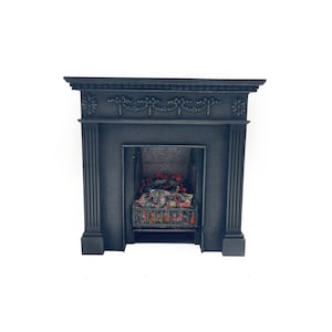 Puede incluir: Chimenea de hierro fundido negro con un diseño decorativo en la parte superior y una rejilla de fuego en el interior. La chimenea está colocada sobre un fondo blanco.