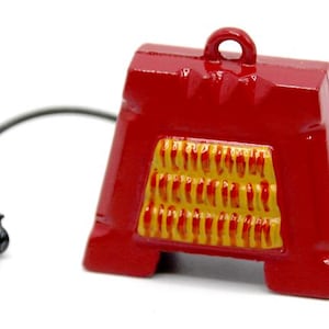 May include: A miniature electric fireplace in red and yellow with a cord and plug. The fireplace has a decorative design with a yellow and red brick pattern.