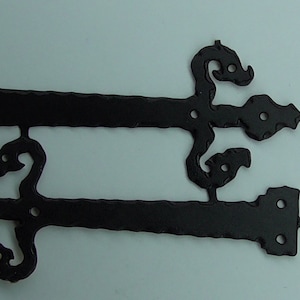 Könnte beinhalten: Zwei schwarze Metallscharniere mit dekorativen Schnörkeln. Die Scharniere sind für den Einsatz an Türen oder Toren konzipiert.