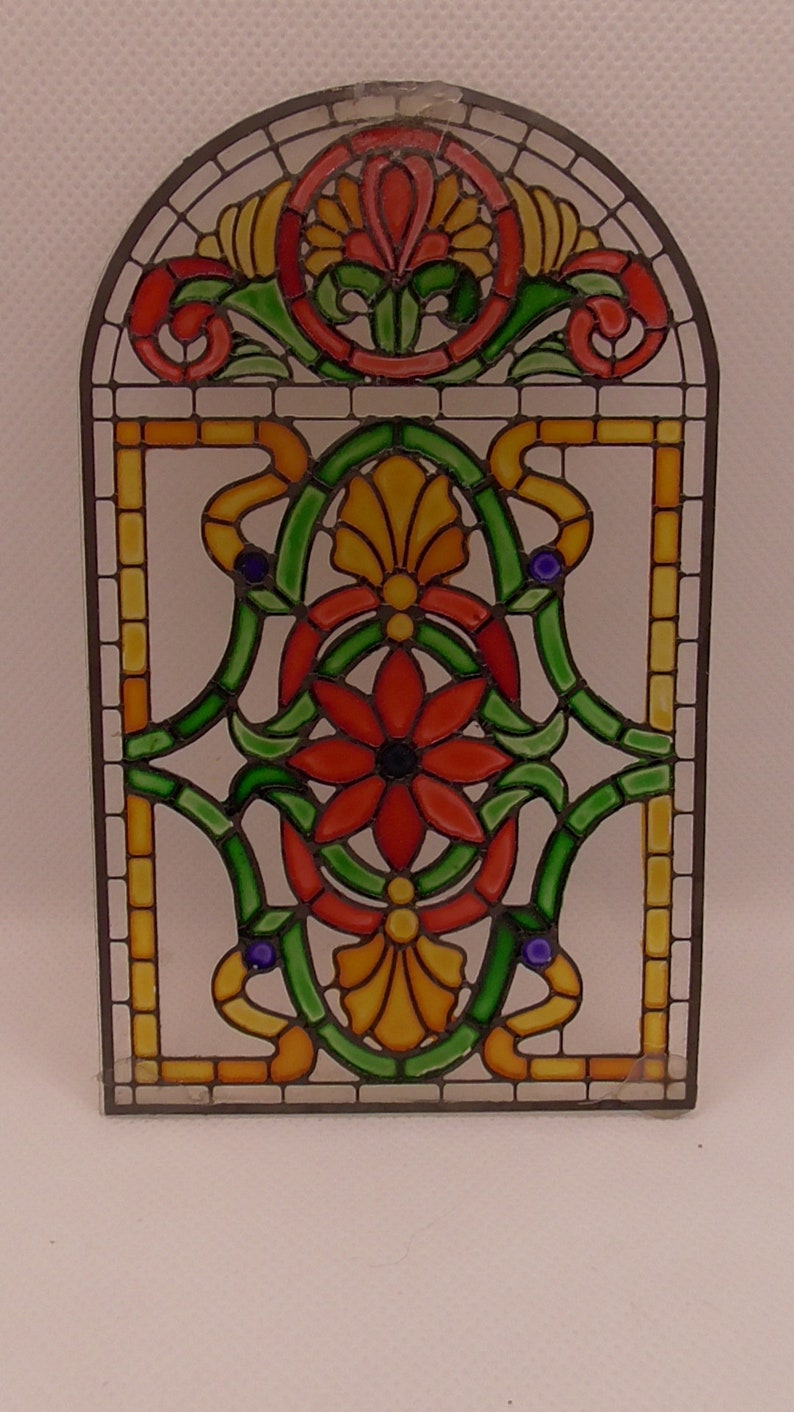 Peut inclure: Un panneau de vitrail avec un motif floral. Le panneau pr&eacute;sente un motif floral rouge, jaune et vert avec un centre bleu. Le panneau est encadr&eacute; d'un cadre en m&eacute;tal noir.