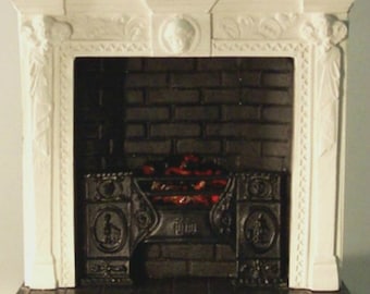May include: White painted miniature fireplace with a black brick surround and a black metal grate. The fireplace has a decorative white mantel with ornate carvings.
