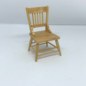 Könnte beinhalten: Ein Miniatur-Holzstuhl mit einem Lattenrücken und einem schlichten Design. Der Stuhl ist aus hellbraunem Holz gefertigt und hat eine natürliche Oberfläche.