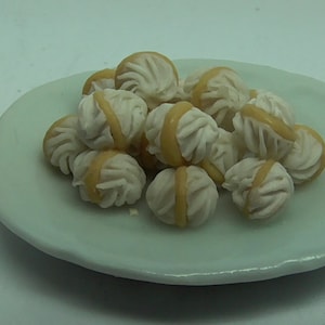 May include: A white plate with a pile of small, white and yellow, cream-filled pastries.