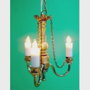 May include: A small, ornate brass chandelier with three candle-shaped lights. The fixture is suspended by a chain and features decorative arms. The background is a solid teal colour.