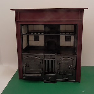 Puede incluir: Una estufa de hierro fundido negro de estilo vintage con dos hornos y un cajón calentador. La estufa tiene un marco de madera rojo y un salpicadero de azulejos blancos.