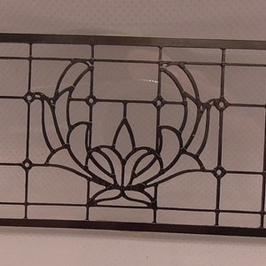 Op de afbeelding: Zwart glas-in-lood raam met een bloemmotief. Het ontwerp heeft een centrale bloem met twee gebogen bladeren aan weerszijden.