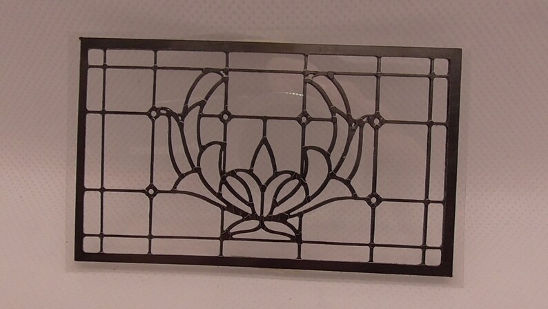 Op de afbeelding: Zwart glas-in-lood raam met een bloemmotief. Het ontwerp heeft een centrale bloem met twee gebogen bladeren aan weerszijden.