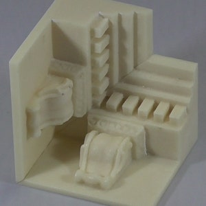 May include: A white plastic model of a corner of a room with a small, detailed, white plastic model of a cash register in the corner.