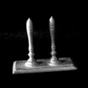 May include: A grayscale image of a vintage ink blotter. The blotter features a rectangular base with two ornate wooden handles. The handles are vertical and have a turned design. The background is black, highlighting the blotter's details.