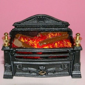 Può includere: Caminetto in ghisa nera con un design decorativo e accenti dorati. Il camino ha un fuoco dall'aspetto realistico con ceppi di colore arancione e marrone.