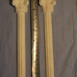 May include: Two white plaster columns with decorative tops, each measuring approximately 23 cm tall, are displayed against a light blue background.