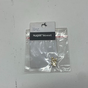 May include: A small clear plastic bag containing several small gold-coloured metal objects. The bag is sealed and attached to a white tag with the text "Maple Street" printed on it. The tag also has the number "302" written on it.