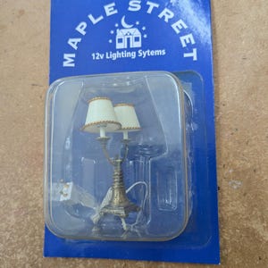 May include: Miniature double lamp with cream shades and a gold-toned base, packaged in a clear plastic case on a blue card. The card reads "MAPLE STREET" and "12v Lighting Systems".