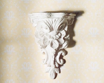 May include: White ornate wall shelf with a floral design. The shelf is made of plaster or ceramic and has a distressed finish.